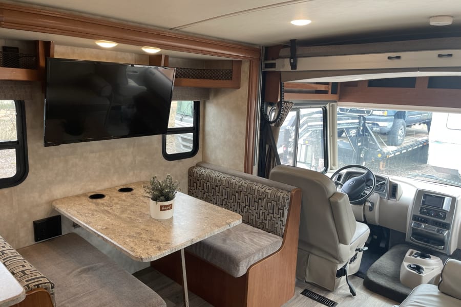 Spacious RV rental interior featuring a dinette with bench seating, wall-mounted TV, and front cockpit area, ideal for travel.