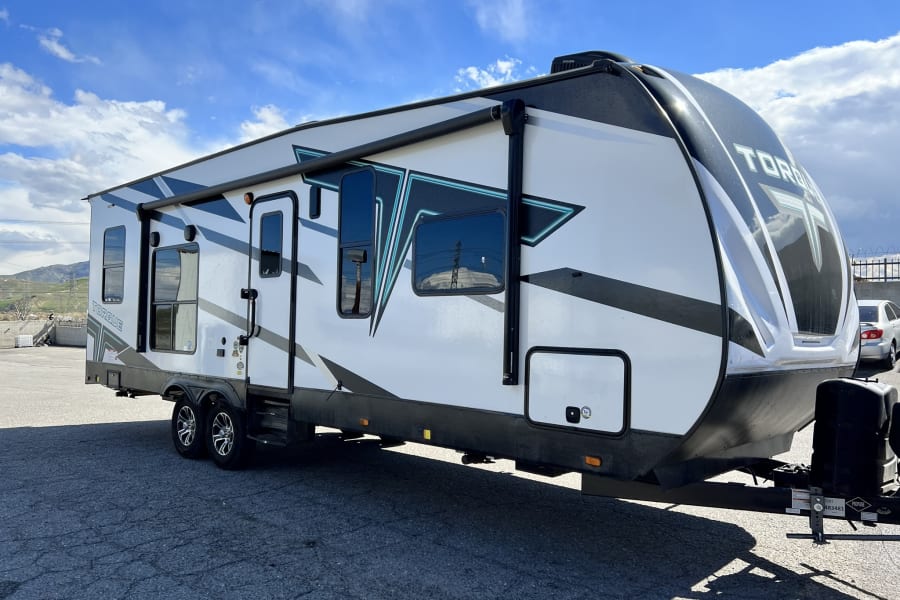 Experience outdoor travel with this white, black, and teal Torque RV rental, featuring an awning and parked under a blue sky.