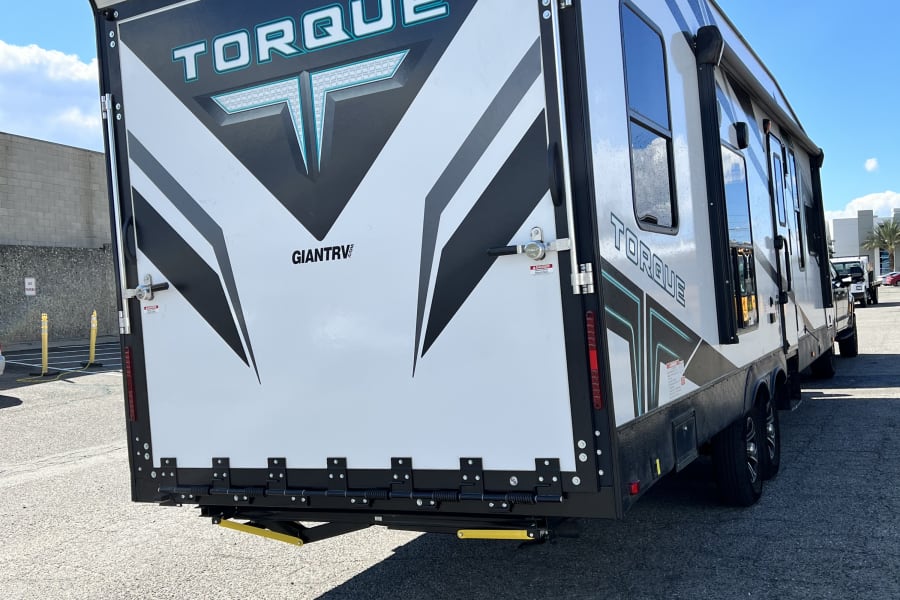 White Torque toy hauler RV rental. Rear view shows large access ramp, black/white graphics, and multiple side windows.