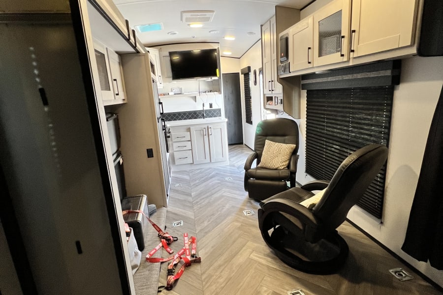 Spacious RV rental interior with modern kitchen, living area, and toy hauler tie-downs on herringbone floor.