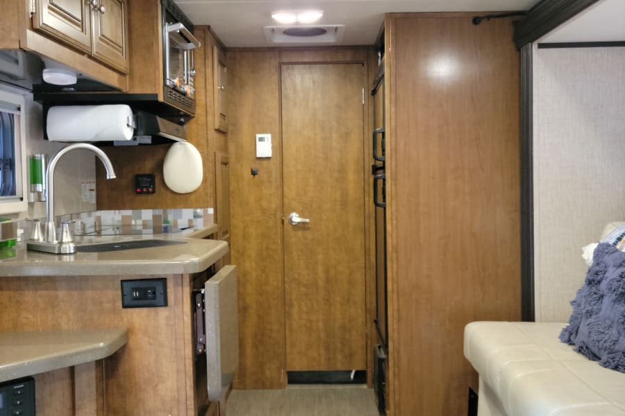 An RV rental's inviting interior: equipped kitchen with sink & microwave, central aisle, cozy bench seating, and ceiling AC.