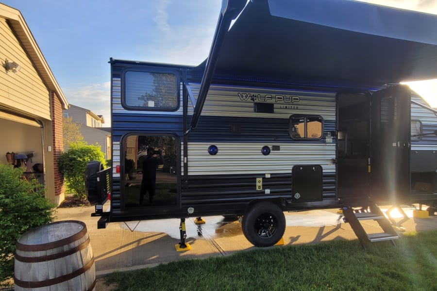 A bright afternoon showcases a parked RV rental, a travel trailer with an extended awning in a home driveway.