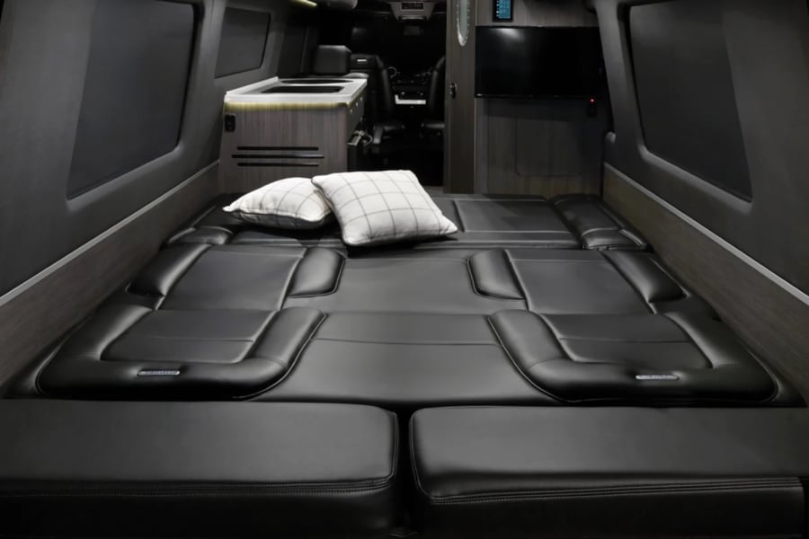 Comfortable black leather bed in an RV rental. Modern camper van interior with kitchenette and TV.