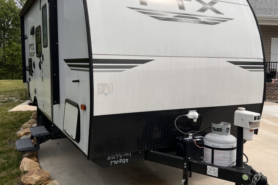 This white travel trailer is parked on a concrete driveway, ready for an RV rental adventure. Visible: propane tank, hitch, steps.
