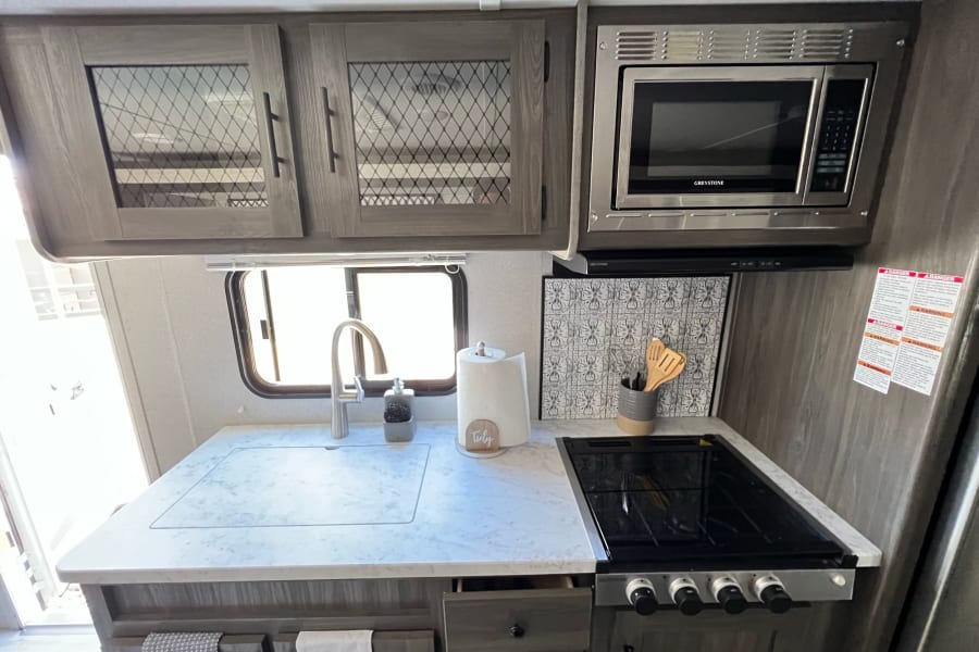 Well-equipped RV rental kitchen featuring a bright counter, sink, stovetop, microwave, and overhead cabinets.