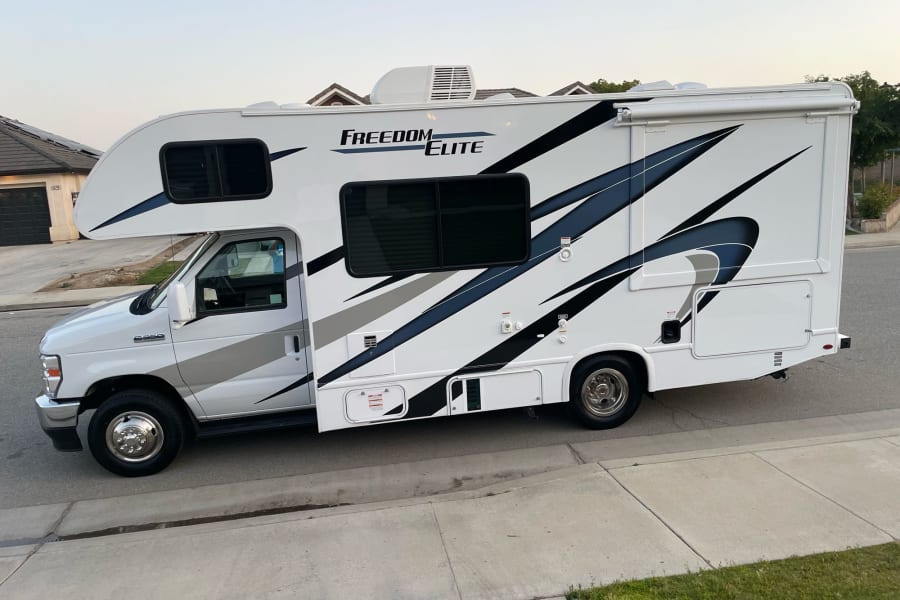 White Freedom Elite RV rental parked on a street, featuring sleek graphics and an awning. Perfect for your next adventure!
