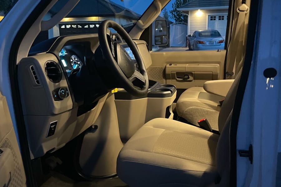 Inside an RV rental van: The well-lit driver's cabin with steering wheel, dashboard, and passenger seats, parked at dusk.