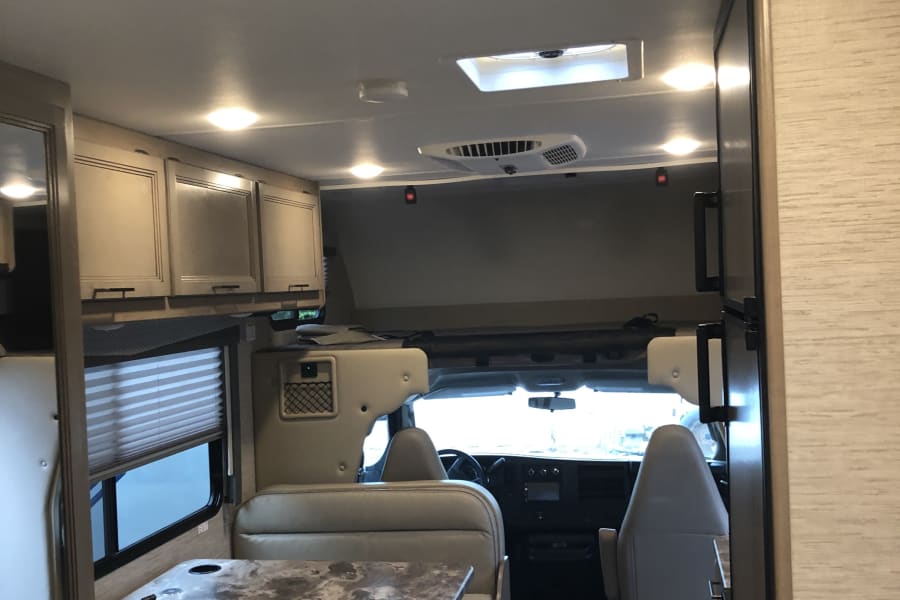 RV rental interior: A modern motorhome's bright living space with a dinette, overhead cabinets, and cockpit view.