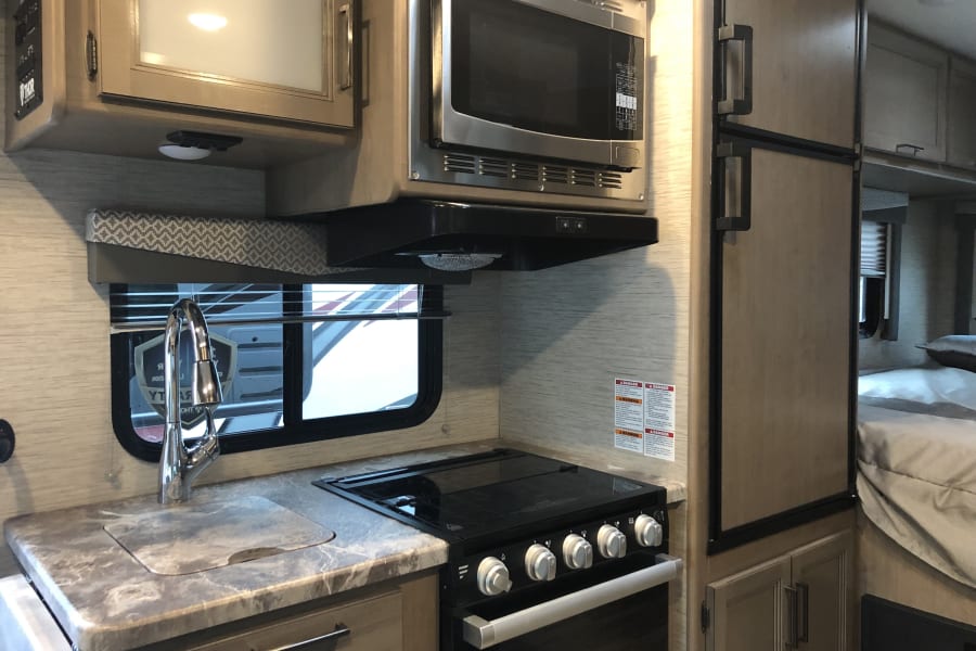 Explore this RV rental's well-appointed kitchen: microwave, stove, sink, & fridge. Comfortable interior for trips.