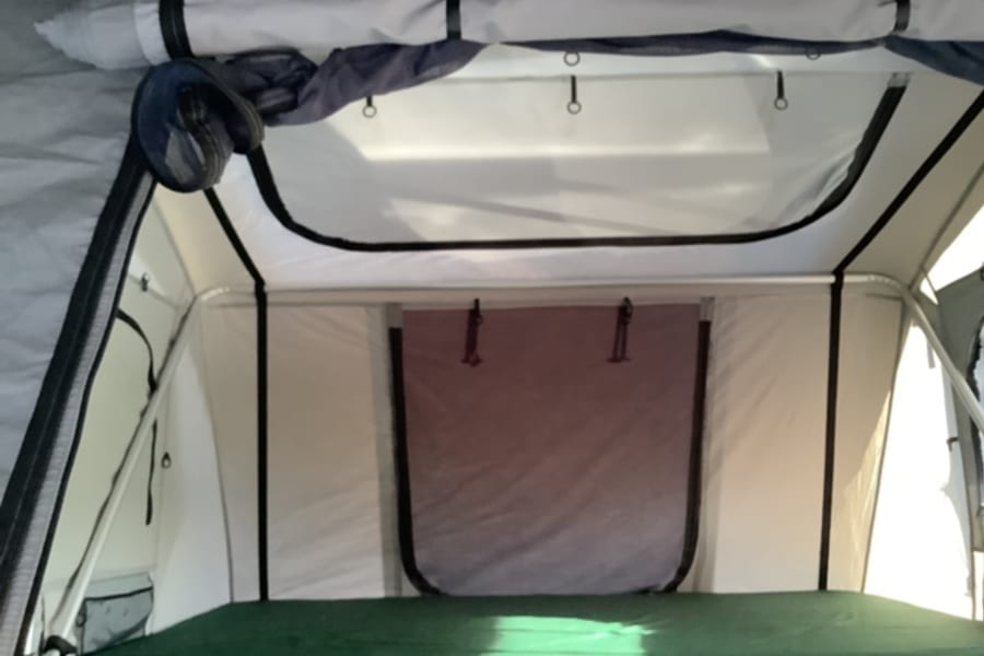 RV rental rooftop tent interior: Bright sleeping area with green mattress & overhead mesh storage. Ideal for camping.