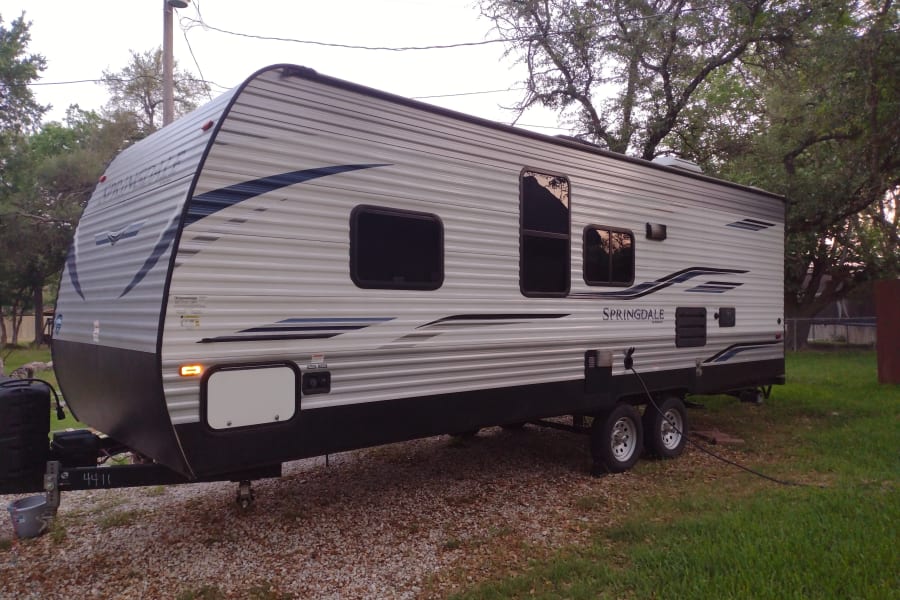 A large, modern white and black Springdale travel trailer, ideal for an rv rental, is parked on gravel beside green grass.