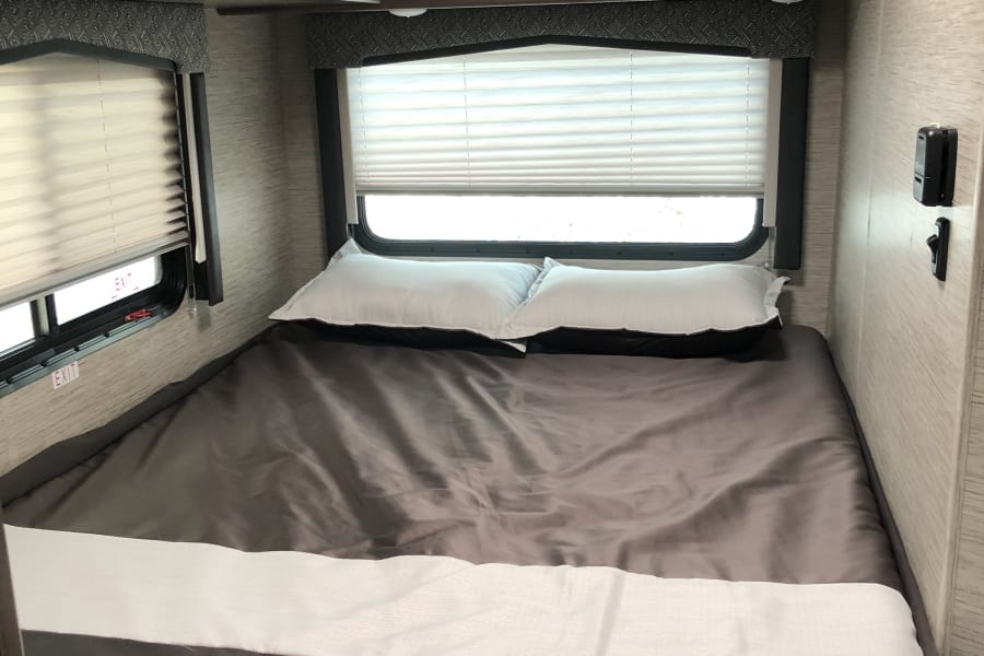 This comfy RV rental bedroom features a neatly made bed, windows with blinds, and practical overhead cabinets.