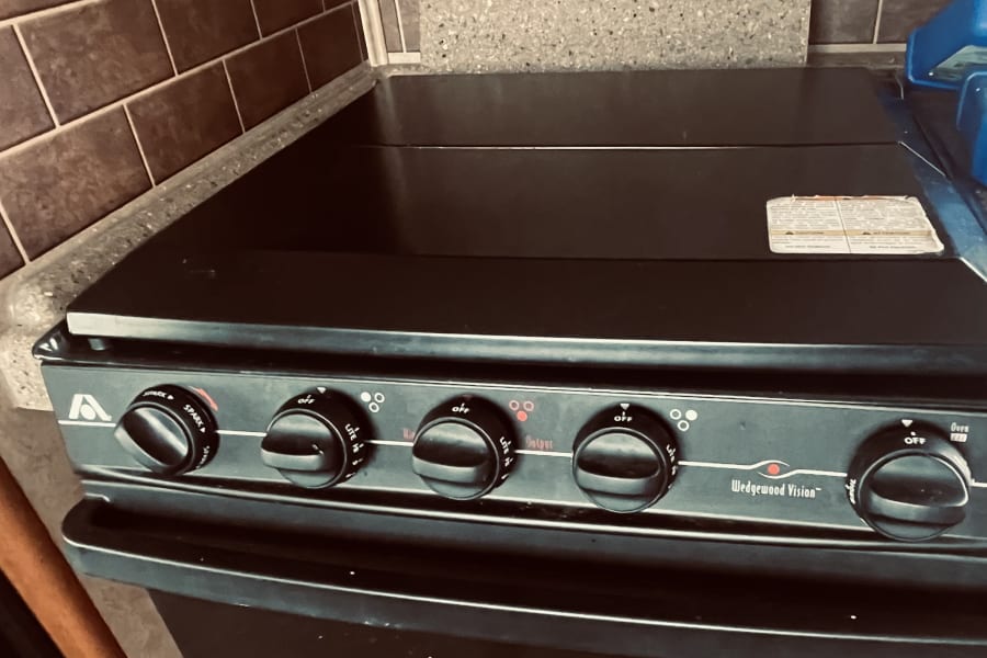 This rv rental's kitchen features a black Wedgewood Vision gas stove with oven, speckled countertop, and tiled backsplash.