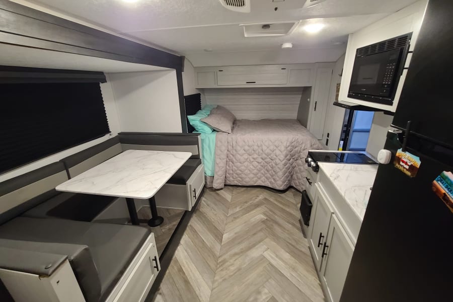 Modern rv rental interior featuring a dinette, cozy bed, and full kitchen with light wood floors.