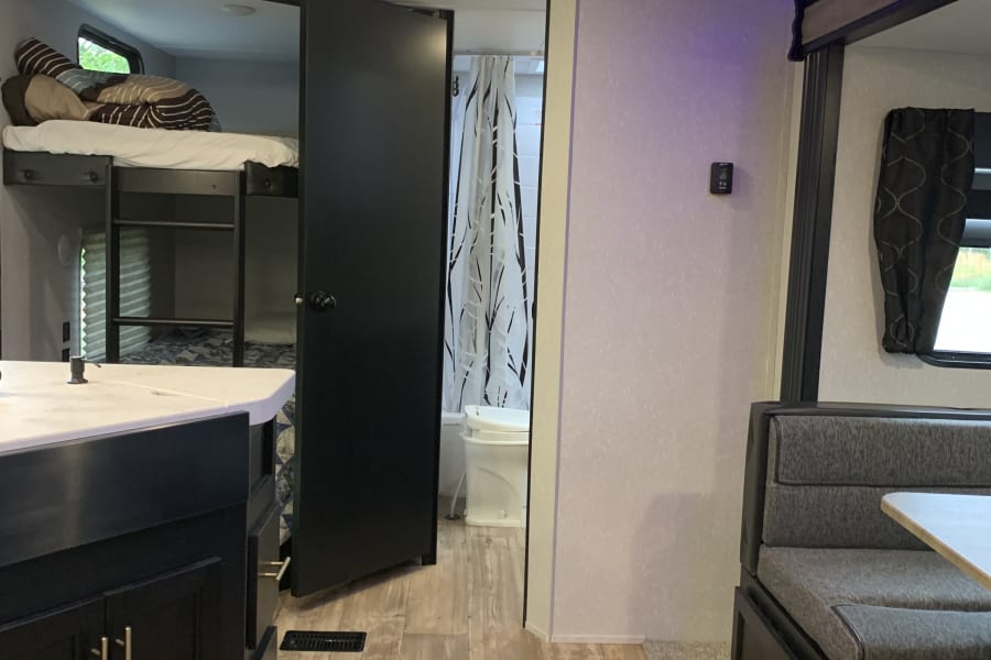 Modern RV rental interior showing a kitchen island, bunk beds, bathroom, and dinette with blue accent lighting.