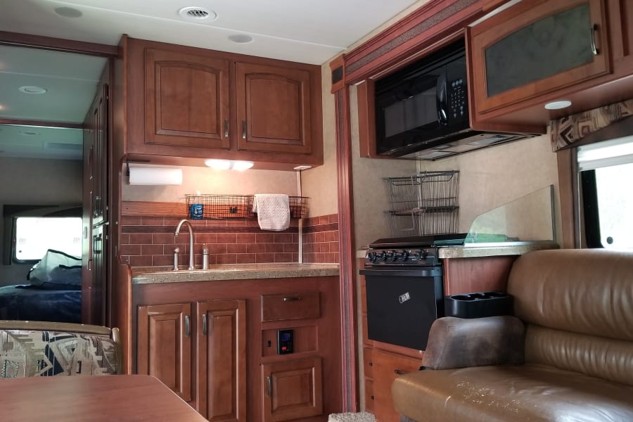 Spacious RV rental interior featuring a full kitchen, living area with sofa, and a glimpse into the bedroom. Ideal for family trips.