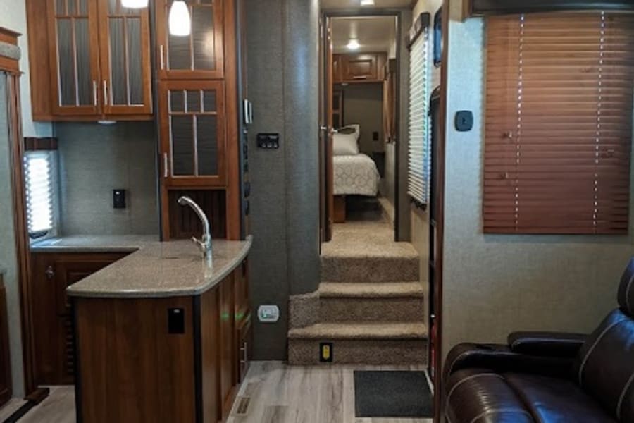 Spacious RV rental interior featuring a kitchen island, living area with sofa, and stairs leading to a cozy bedroom.