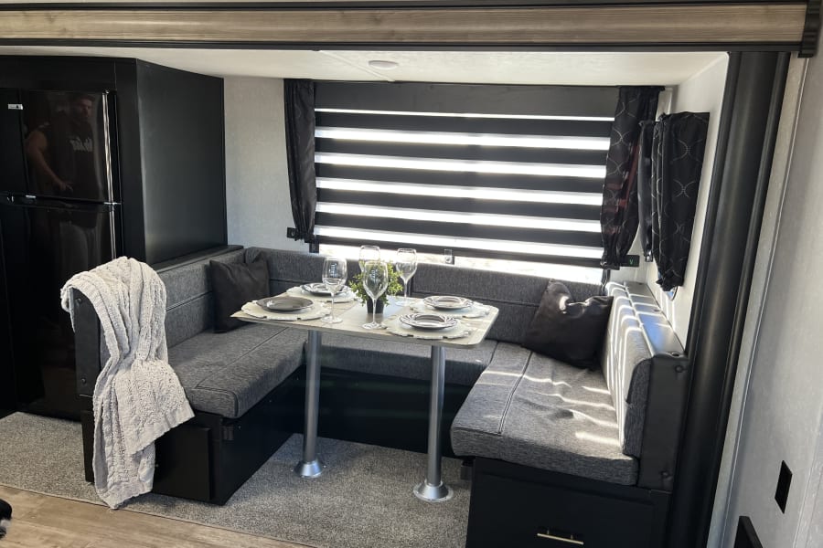 Modern RV rental interior: U-shaped dinette with table set for dining, adjacent to a sleek black refrigerator.