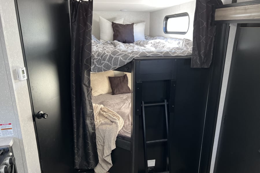 Inside an RV rental, discover comfortable bunk beds with patterned bedding, privacy curtains, and a ladder. Black and white decor.