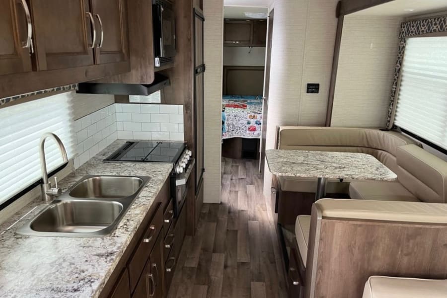 Inside an RV rental: full kitchen with granite counters, U-shaped dinette, and bed area.