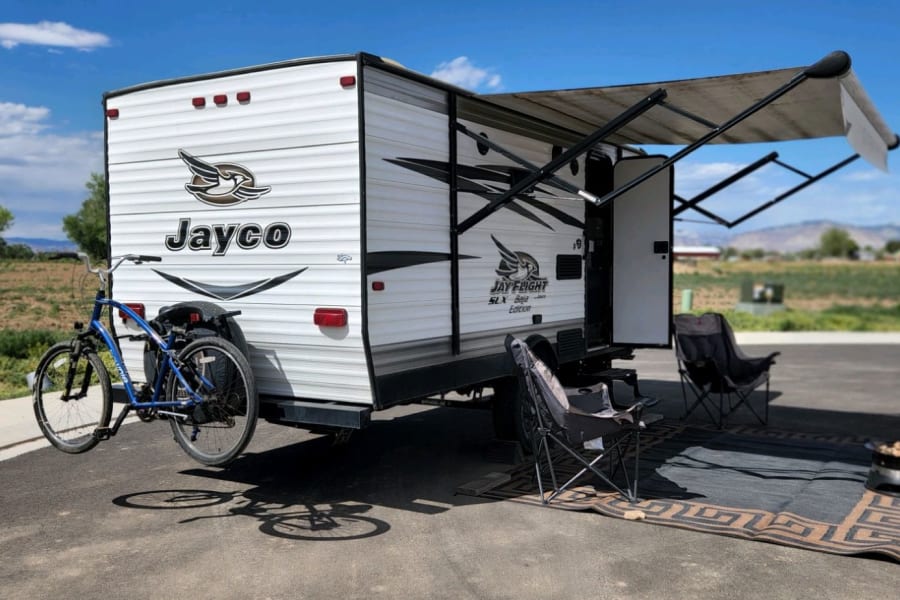 Perfect day for an RV rental adventure! Jayco travel trailer, bike, awning, and camp chairs ready for relaxation.