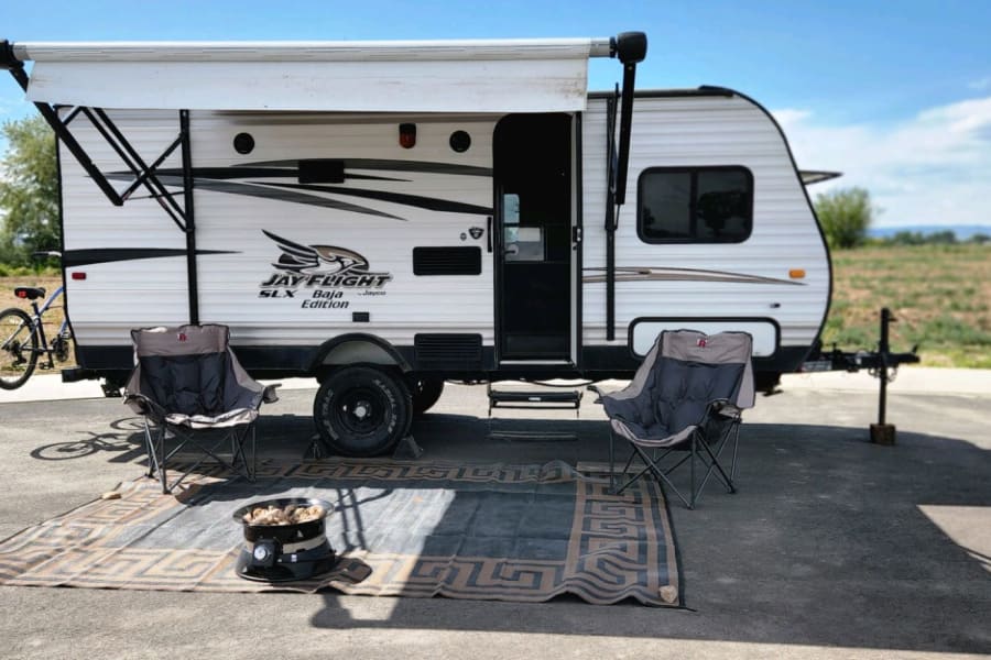 RV rental travel trailer with awning, outdoor chairs, mat, and fire pit. Perfect for camping adventures.