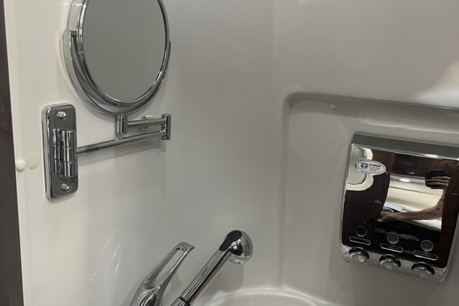 Compact RV rental wet bath: white molded unit with sink, pull-out faucet/shower, magnifying mirror, and multi-dispenser.
