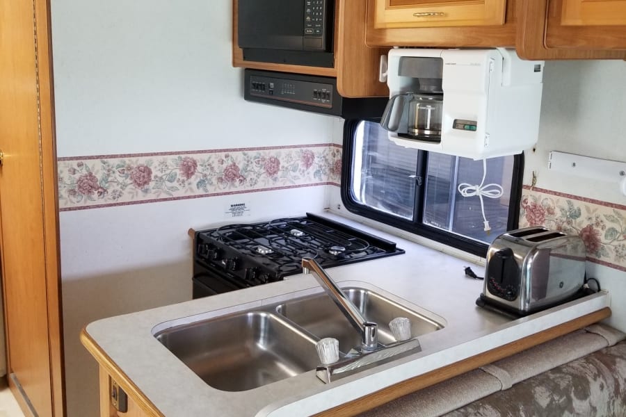 RV rental kitchen featuring a sink, stove, microwave, coffee maker, and patterned dining booth.