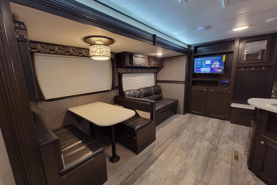 Spacious RV rental interior featuring a comfortable dinette, sofa, and entertainment center in a well-appointed living space.