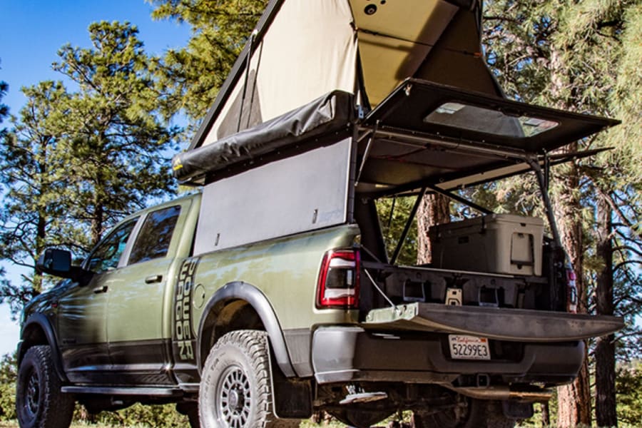 This rugged olive green overlanding truck, with a deployed rooftop tent & bed storage, is an ideal RV rental for wilderness adventures.