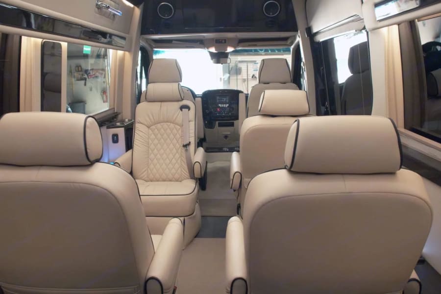 View of a high-end RV rental interior, featuring multiple rows of cream leather captain's chairs.