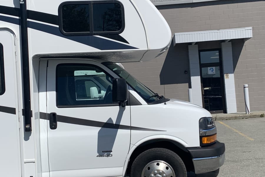 A white motorhome RV rental is parked at the Alaska RV Rentals building under a sunny sky.