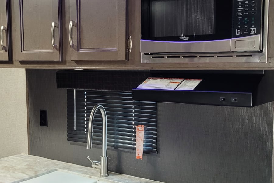 Well-equipped RV rental kitchen: stainless microwave, white sinks, gas oven, and cool blue accent lights.