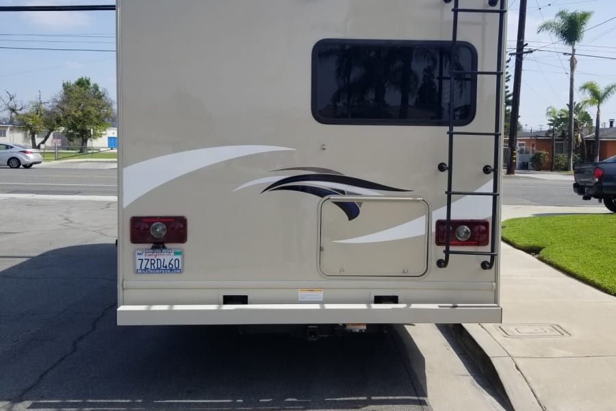 Rear view of a beige RV rental, featuring a ladder and CA license plate, parked on a sunny street.
