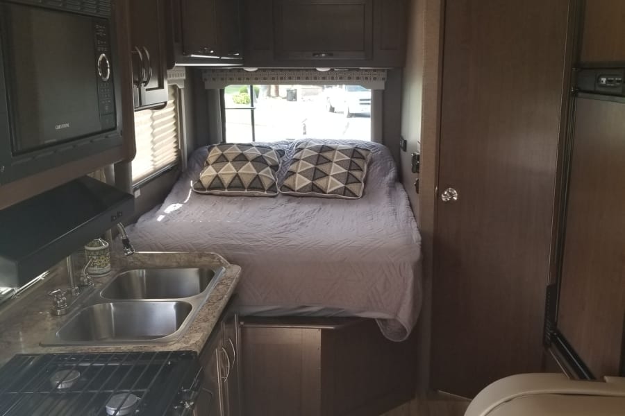 Explore this RV rental's well-equipped interior: kitchen, microwave, stove, sink, comfortable bed, and fridge.