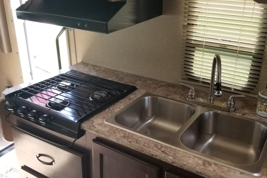 Compact RV rental kitchen featuring a gas stove, microwave, double sink, and storage cabinets, ideal for road trips.
