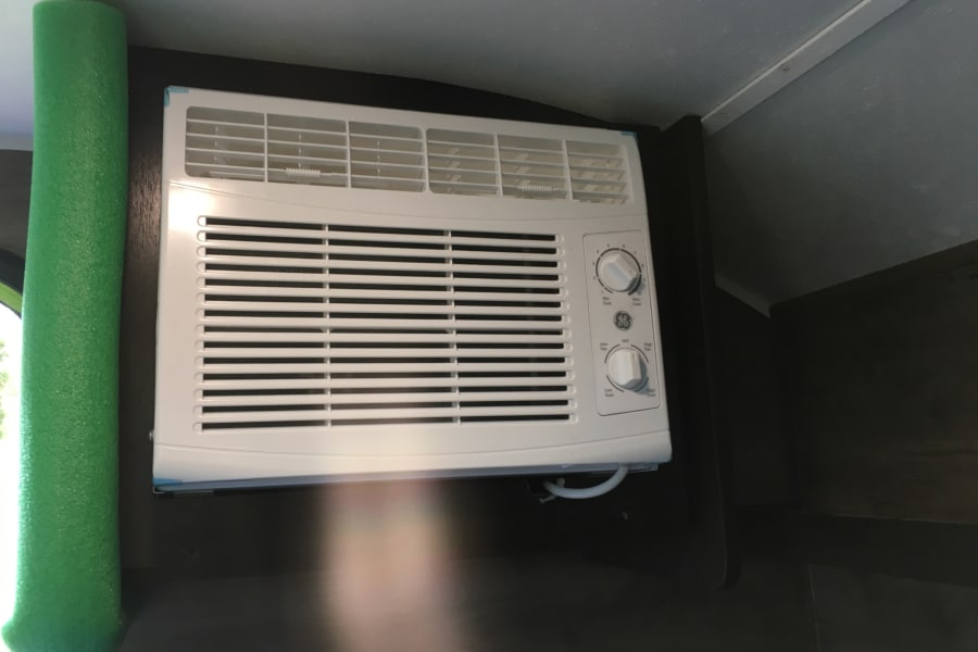 White GE air conditioner with control knobs and green foam insulation, seen inside an RV rental for cooling comfort.