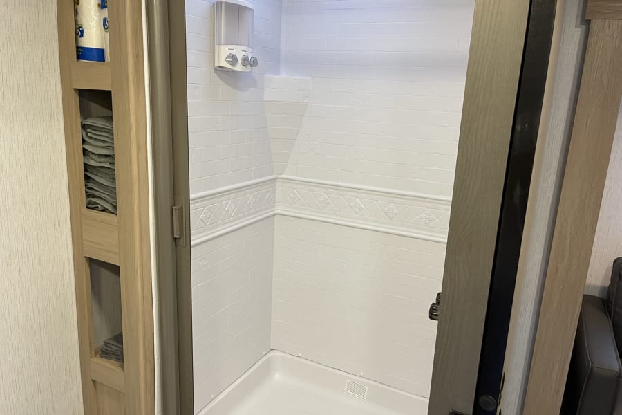 Inside an RV rental: a compact, clean bathroom featuring a white-tiled shower with dispenser & built-in storage.