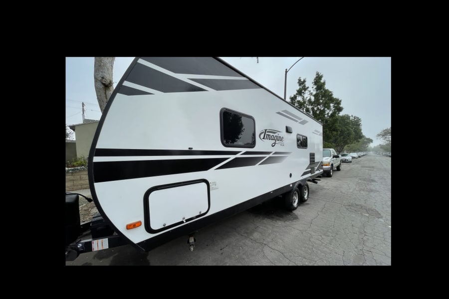 A white Imagine XLS travel trailer with black graphics is parked on a street. Perfect for your next rv rental adventure!