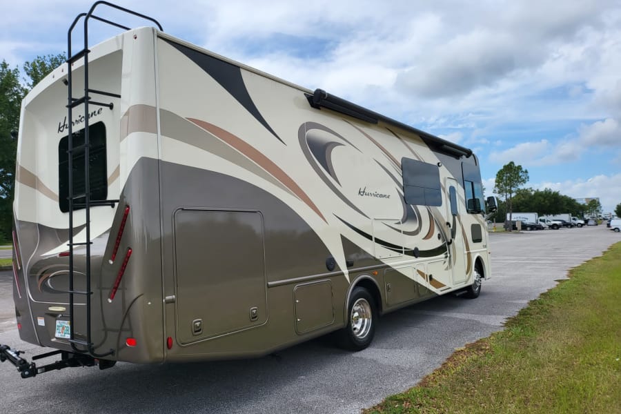 Explore with this Class A RV rental, beige with brown graphics, featuring an awning and rear ladder. Ready for travel.