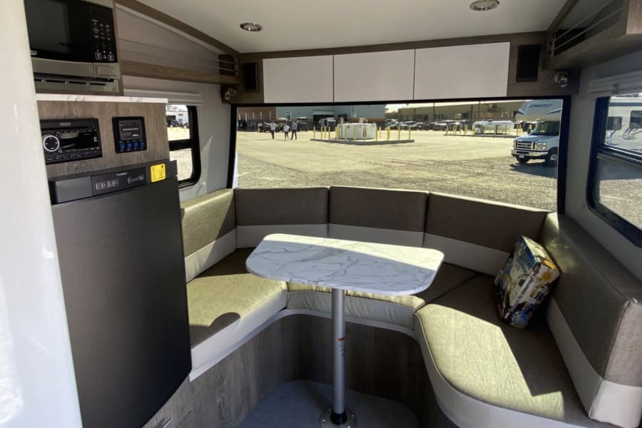 Modern RV rental interior: U-shaped dinette, compact kitchen with microwave & fridge, overhead cabinets. Bright, functional space.