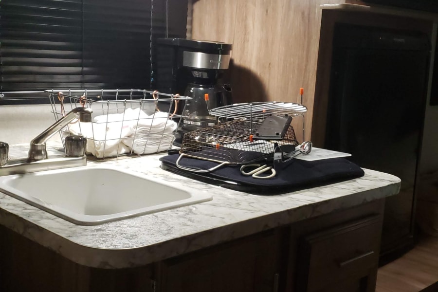 An inviting rv rental kitchen boasts a sink, coffee maker, microwave, and refrigerator, with warm wood cabinets & modern counters.