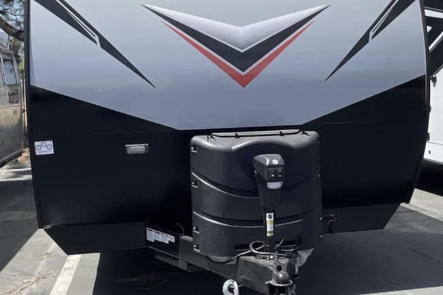 Front of a gray and black Shockwave travel trailer, ready for rv rental. Propane tank and hitch visible.