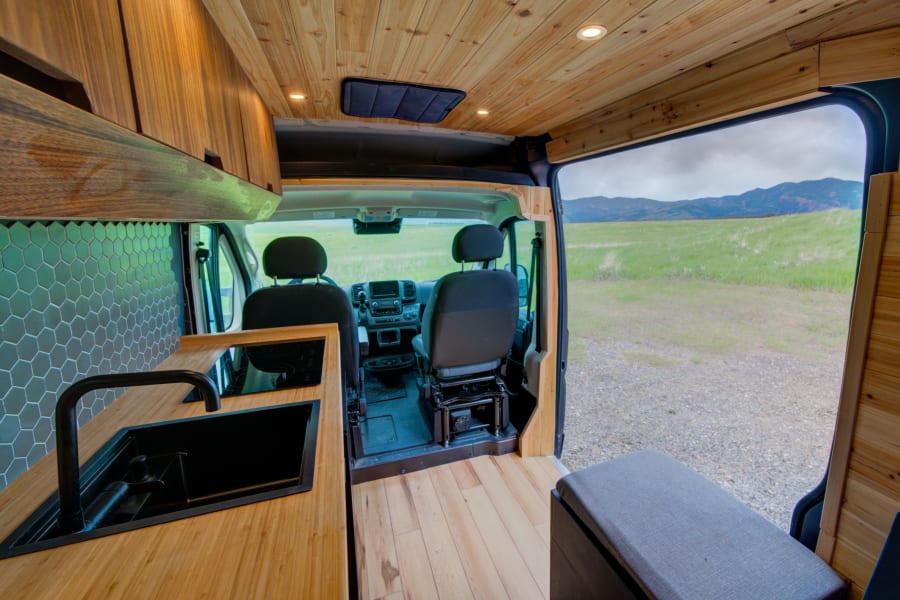 Spacious RV rental interior with a modern kitchen, wood paneling, and an inviting view of green fields and mountains.