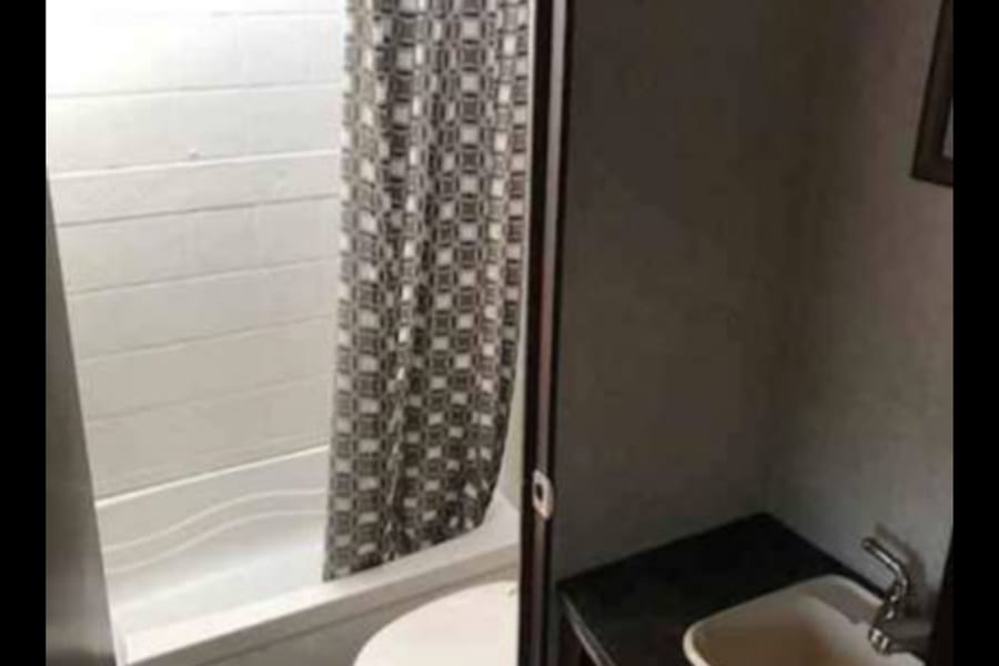 Compact RV rental bathroom showing a shower/tub, toilet, and sink vanity with dark countertop.