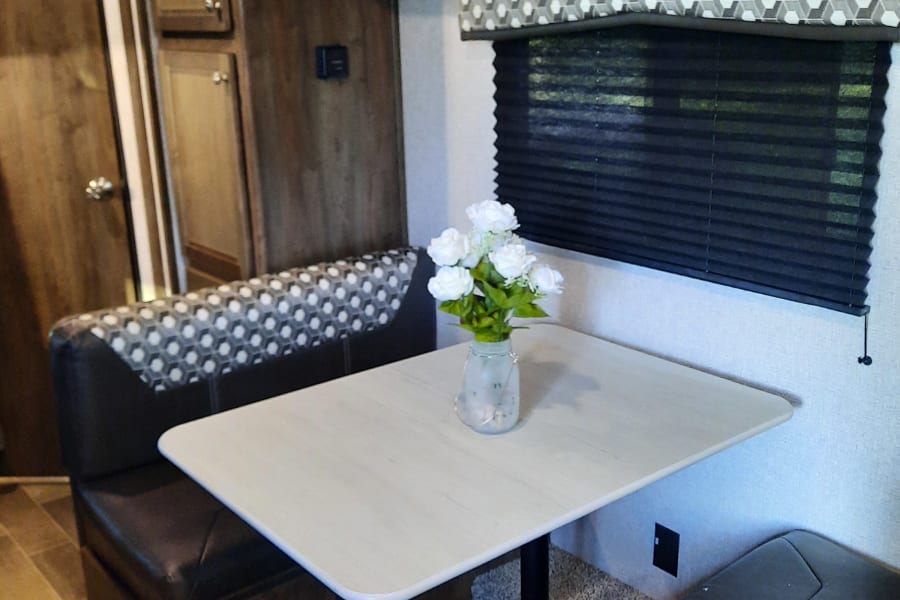 Inside this RV rental: a comfortable dinette with patterned bench seating, a table, and wooden cabinets.