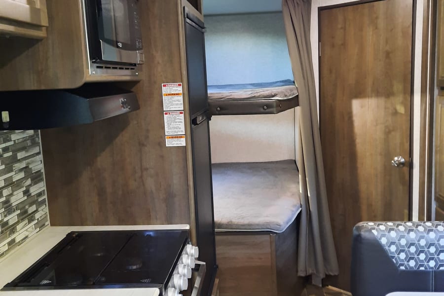 RV rental: Interior view of compact living space featuring kitchen with microwave, stove, dinette, and wall-mounted AC.