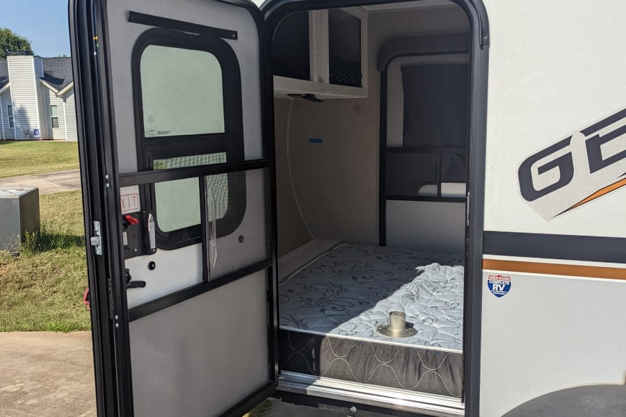 This rv rental, a compact travel trailer, welcomes you with its open door revealing a cozy bed for your next adventure.
