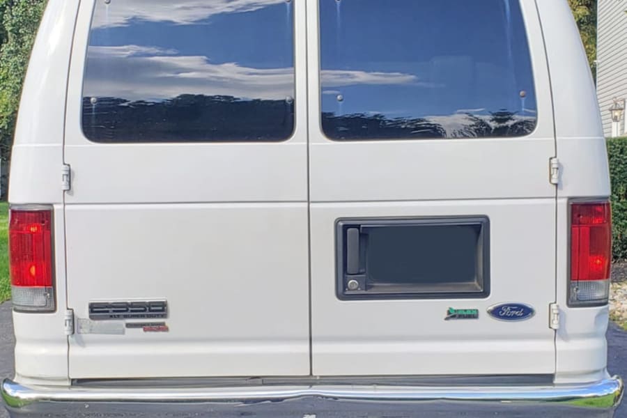 Rear view of a white Ford E-350 van, perfect for an RV rental. Features twin rear doors, large windows, and a chrome bumper.