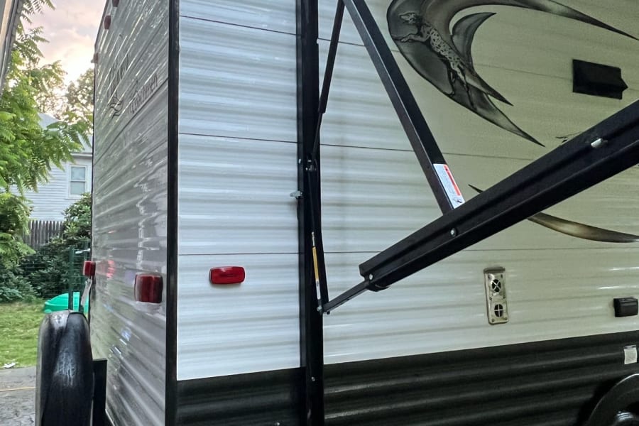 Exterior view of a travel trailer with an extended awning & rear spare tire, perfect for an rv rental.